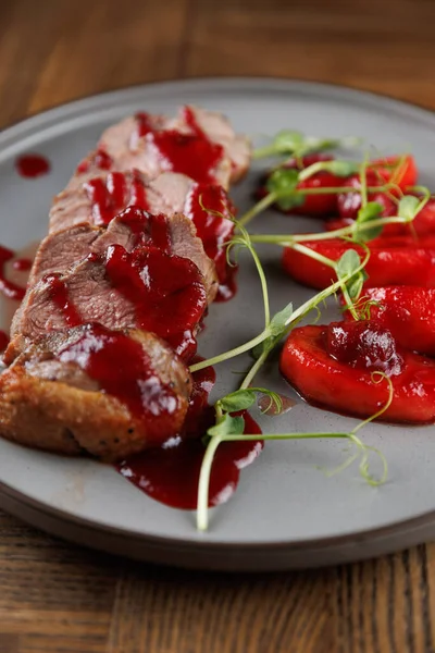 İyi sunulmuş bir tabakta, gri bir tabakta taze çileklerin yanında kırmızı sosla serpiştirilmiş et yer alıyor. Yemek canlı renkler ve dokular sergiliyor..