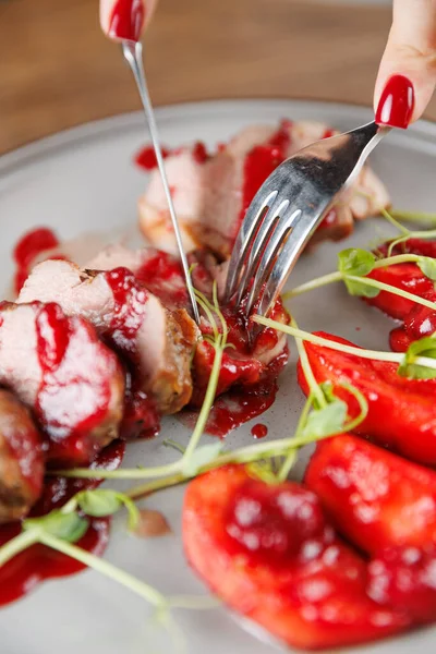 Bir insan, içinde kırmızı sosla kaplanmış et dilimlerinin olduğu bir tabağı keser. Yanında da yemek masasında taze meyve olur..