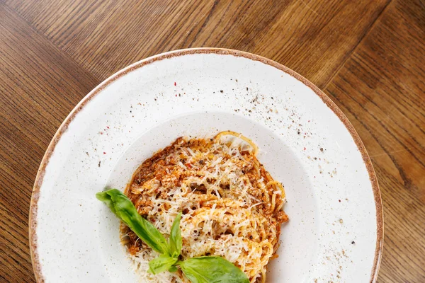 Zengin soslu ve rendelenmiş peynirli spagetti ahşap bir masada beyaz bir kasede oturur. Taze bir fesleğen yaprağı yemeğe bir renk katar. Her yemek için mükemmel..