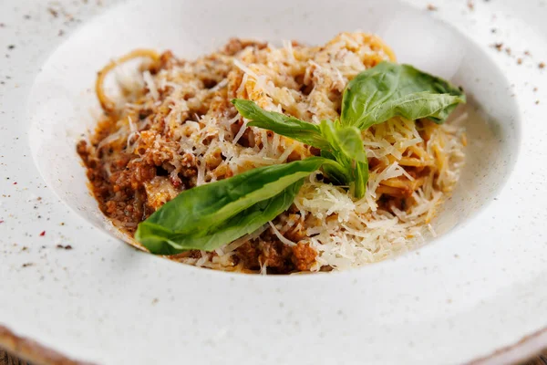 Bir kase et soslu spagetti, rendelenmiş peynir serpiştirilmiş ve taze fesleğen yapraklarıyla süslenmiş. Bu yemek lezzet ve dokuların bir karışımını sergiler..