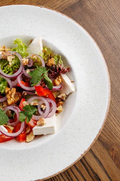 Renkli bir salata dilimlenmiş tavuk, marul, domates, soğan ve ceviz içerir. Kişniş ile süslenir ve ahşap bir masada yuvarlak bir tabakta sunulur..