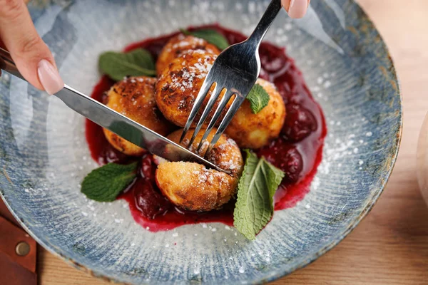 Elleri çatal ve bıçak ile pudra şekeri ile kaplanmış altın hamur işlerini kesmek için, canlı kiraz sosu ve taze nane ile çevrili. Sahne, aşçılık deneyimini yakalar..