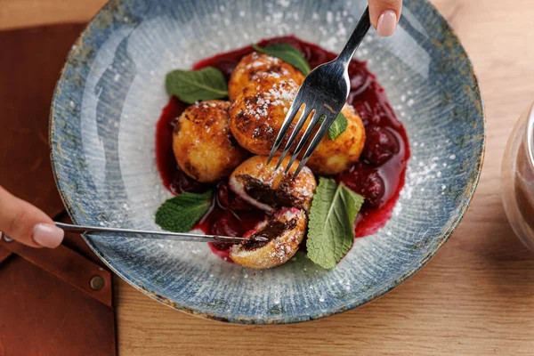 Kızarmış hamur topları tatlı dolguyu ortaya çıkarmak için kesilir. Çilek sosu ve nane yapraklarıyla mavi bir tabakta servis edilir ve Ukrayna aromalı tatlar davetkar bir sunumda vurgulanır..