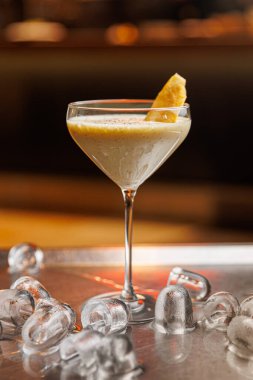 Bir kokteyl, buzla çevrili metal bir masanın üzerindeki bir bardağa yerleştirilir. İçki bir meyve garnitürüyle kaplıdır. Sıcak bir atmosfer yemek deneyimini arttırır..