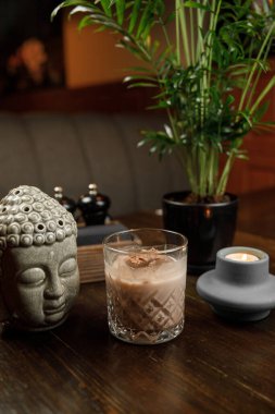 Bir tatlı içeceği bir bitki ve mumun yanındaki masada oturur. Bir Buda heykeli süs katar. Ortam sıcak ve davetkar, rahatlamak için mükemmel..