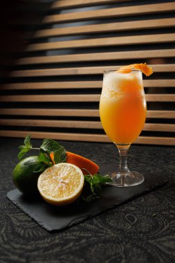 Bir bardak turunçgil içeceği siyah bir levhada duruyor. Limon ve limon yakınlarda, yanında taze nane yaprakları var. Arka planda ahşap çizgiler var..