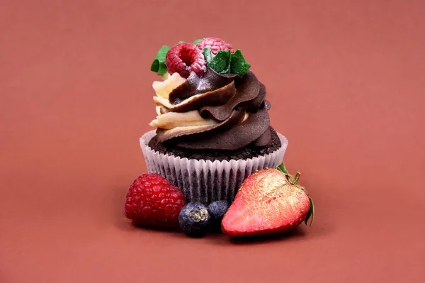 ラズベリーのあるチョコレートバニラカップケーキはまだストック画像を生きています 茶色の背景の写真に隔離された果物とおいしいクリーミーなカップケーキ ベリーストック画像付きフレッシュカップケーキ — ストック写真