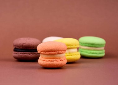 Kahverengi arka planda renkli makaronlar. Renkli Fransız badem kurabiyeleri, metin için kopyalama alanı olan kahverengi bir arkaplanda izole edilmiş.