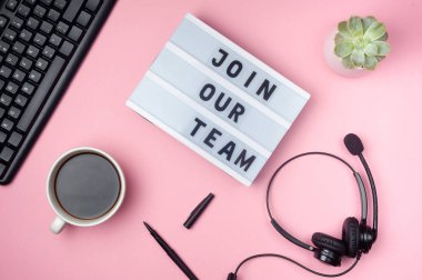 Ekibimize katıl. Işık kutusundan mesaj at. Düz konum - klavye, kahve, kulaklık ve pembe arka planda kalem. Üst Manzara. İş yeri kavramı. 