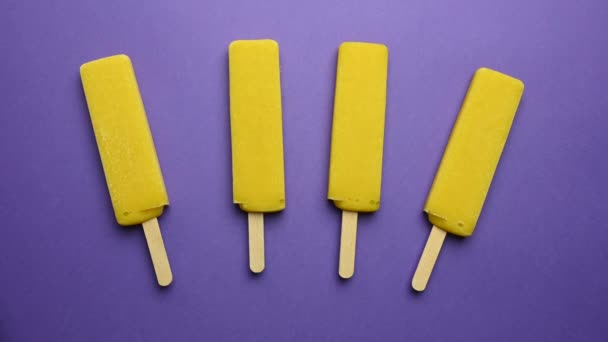 Yellow ice cream on a stick mango sorbet melts on a purple background. Time lapse — Stock Video