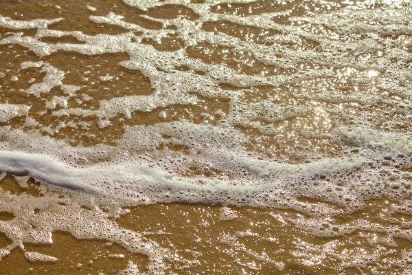 Seafoam em uma praia arenosa — Fotografia de Stock