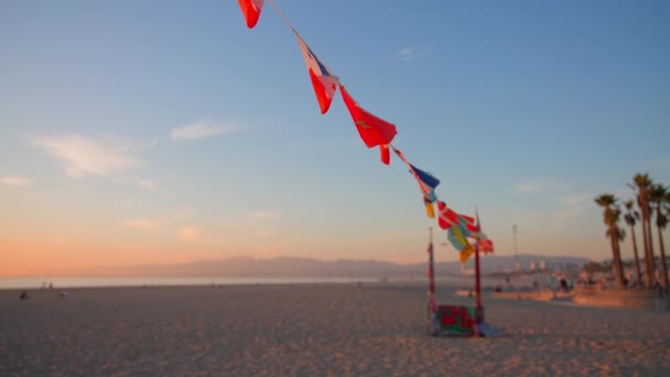 Los angeles, kalifornien, usa - 10. Dezember 2020: venedig ocean beach skatepark. Kleine Fahnen wehen im Wind auf einem Seil, im Hintergrund der Sommersonnenuntergang. Zeitlupe. — Stockvideo