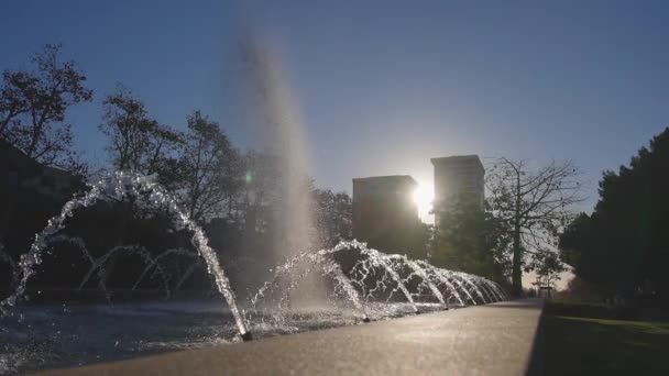 Piękna fontanna w słoneczny dzień w zwolnionym tempie. Dysze wody lśnią w słońcu. Jasne plamy powoli rozprzestrzeniają się na boki.. — Wideo stockowe