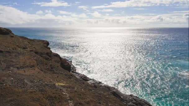 Solopgang over øen Oahu. Hvide skyer svæver hen over den blå himmel. Blue Waves of te Pacific Ocean slår Oahu Island vulkanske klipper. Turkis vand farve. En klar solskinsdag. DCI 4k – Stock-video