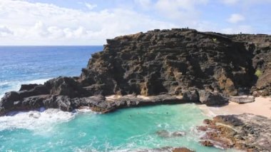 People swim in the turquoise waters of the Tropical Beach. Halona Beach Cove. Blue Waves of the Pacific Ocean Beats Oahu Island Volcanic Cliffs. Clear sunny day. DCI 4k