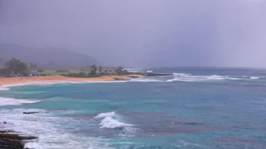 People swim in the turquoise waters of the Tropical Beach. Sandy Beach. Blue Waves of the Pacific Ocean Beats Oahu Island Volcanic Cliffs. Ke One Kula Lookout. Clear sunny day. DCI 4k