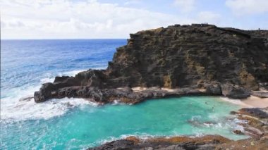 People swim in the turquoise waters of the Tropical Beach. Halona Beach Cove. Blue Waves of the Pacific Ocean Beats Oahu Island Volcanic Cliffs. Clear sunny day. DCI 4k