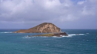 Tavşan Adası manzarası. Pasifik Okyanusu 'nun dalgaları tropikal kumsalın sarı kumlarını silip süpürüyor. Hawaii 'nin muhteşem dağları Oahu adasına karşı beyaz bulutlu mavi gökyüzü..