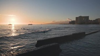 Tropik bir günbatımının inanılmaz renkleri. Okyanus ufkunda yüzen yelkenli teknelerinin siluetleri. Sörfçüler dalgalara biner. Oahu, Hawaii 'de yaz tatili. Yavaş çekim.