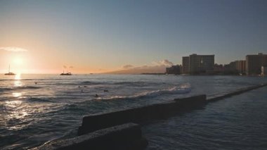 Tropik bir günbatımının inanılmaz renkleri. Okyanus ufkunda yüzen yelkenli teknelerinin siluetleri. Sörfçüler dalgalara biner. Oahu, Hawaii 'de yaz tatili. Yavaş çekim.