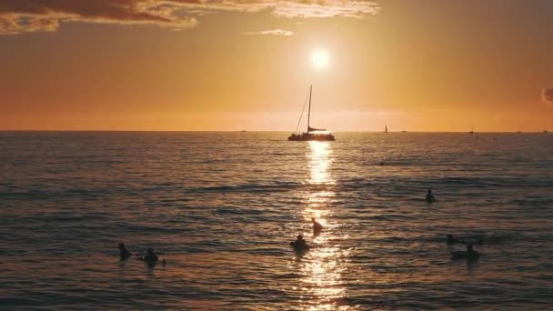 Geweldige kleuren van een tropische zonsondergang. Silhouetten van zeilboten die aan de oceaanhorizon drijven. Surfers rijden op de golven. Oahu, zomervakantie op Hawaï. Langzame beweging. — Stockvideo