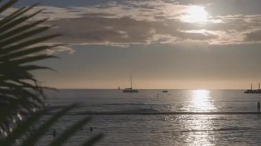 Tropik bir günbatımının inanılmaz renkleri. Okyanus ufkunda yüzen yelkenli teknelerinin siluetleri. Sörfçüler dalgalara biner. Oahu, Hawaii 'de yaz tatili..