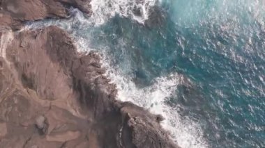 İHA 'dan hava görüntüsü. Kayalık okyanus kıyısının en üst manzarası. Kamera 360 derece dönüyor. Pasifik Okyanusu 'nun Mavi Dalgaları kayaya çarpıyor. Beyaz deniz köpüğü. Tropik ada Oahu Hawaii 'nin volkanik plajı.