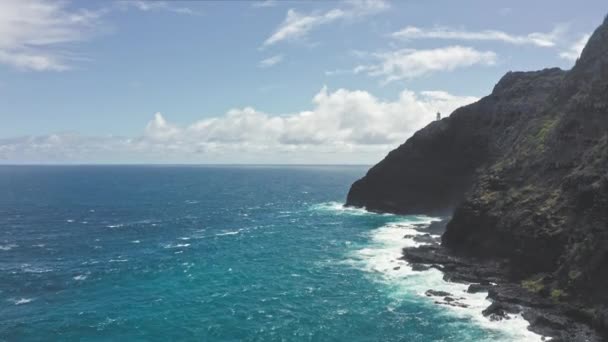 Létající dron nad oceánem. Pohled na maják Makapuu. Vlny Tichého oceánu omývají skalnatý břeh. Nádherné hory havajského ostrova Oahu na pozadí modré oblohy s bílými mraky. — Stock video
