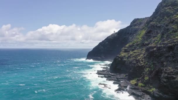Volando drone sobre el océano. Vista del faro de makapuu. Las olas del Océano Pacífico lavan la orilla rocosa. Magníficas montañas de la isla hawaiana de Oahu contra el telón de fondo del cielo azul con nubes blancas. — Vídeos de Stock