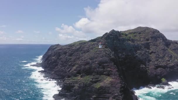 Létající dron nad oceánem. Pohled na maják Makapuu. Vlny Tichého oceánu omývají skalnatý břeh. Nádherné hory havajského ostrova Oahu na pozadí modré oblohy s bílými mraky. — Stock video
