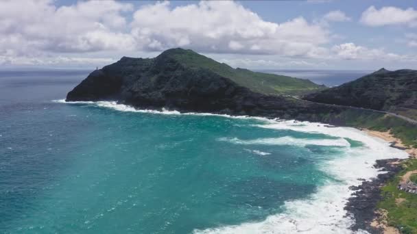 Volando drone sobre el océano. Vista del faro de makapuu. Las olas del Océano Pacífico lavan la orilla rocosa. Magníficas montañas de la isla hawaiana de Oahu contra el telón de fondo del cielo azul con nubes blancas. — Vídeos de Stock