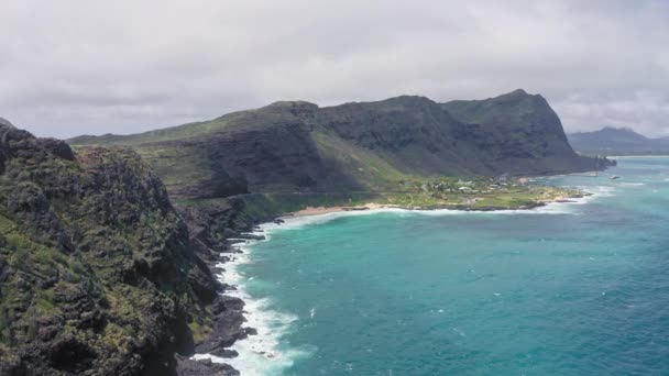 Volando drone sobre el océano. Disparando desde una vista de pájaro. Las olas del Océano Pacífico lavan la orilla rocosa. Magníficas montañas de la isla hawaiana de Oahu contra el telón de fondo del cielo azul con nubes blancas. — Vídeos de Stock