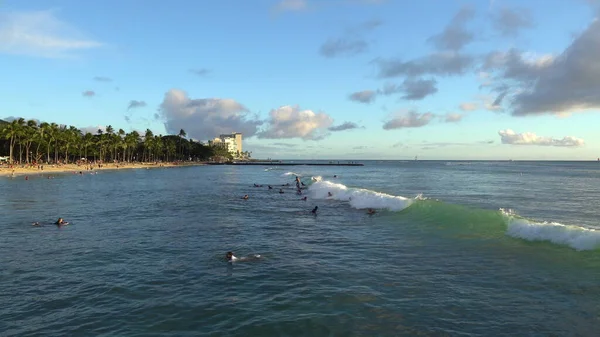 Honolulu, Hawaii - 15. März 2021: Herrlicher Sonnenuntergang am Strand von Honolulus Waikiki. Surfer reiten auf den Wellen. Touristen sonnen sich am Strand. — Stockfoto