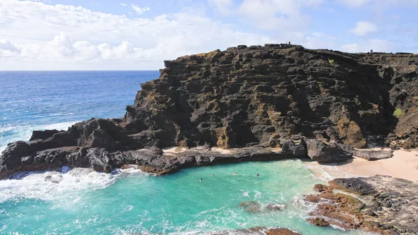 People swim in the turquoise waters of the Tropical Beach. Halona Beach Cove. Blue Waves of the Pacific Ocean Beats Oahu Island Volcanic Cliffs. Clear sunny day. DCI 4k — Zdjęcie stockowe