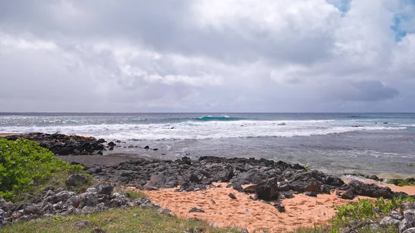 Błękitne fale Pacyfiku toczą się nad skalistą plażą hawajskiej wyspy Oahu. Zielone tropikalne drzewo pod jasnym letnim słońcem przeciwko błękitnemu niebu z białymi chmurami. — Zdjęcie stockowe