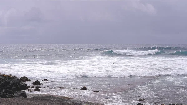A Csendes-óceán kék hullámai gurulnak át a Hawaii-sziget sziklás partján, Oahuban. A fényes nyári nap alatt, a kék ég ellen, fehér felhőkkel.. — Stock Fotó