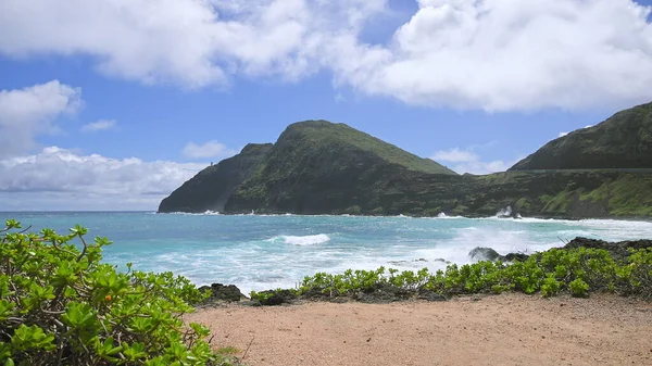 Uitzicht op makapuu vuurtoren. Golven van de Stille Oceaan spoelen over geel zand van tropische strand. Prachtige bergen van het Hawaïaanse eiland Oahu tegen een achtergrond van blauwe lucht met witte wolken. — Stockfoto