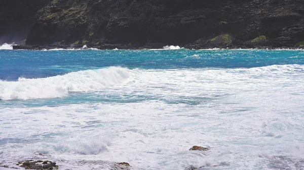 Błękitne fale Oceanu Spokojnego pokonują wulkaniczne klify wyspy Oahu. Turkusowy kolor wody. Jasne, słoneczny dzień. Archipelag Hawajów. Nadkomisarz 4k. Zwolniony ruch. — Zdjęcie stockowe