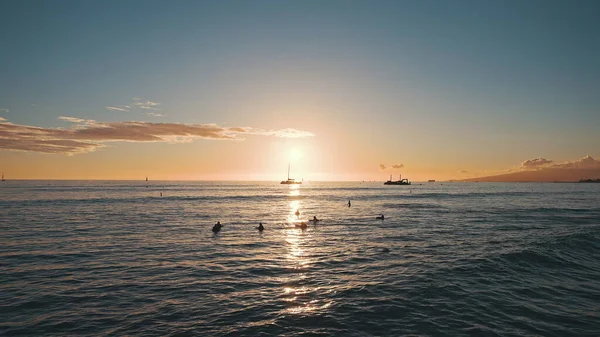 Erstaunliche Farben eines tropischen Sonnenuntergangs. Silhouetten von Segelbooten, die am Horizont des Ozeans schwimmen. Surfer reiten auf den Wellen. Oahu, Sommerurlaub auf Hawaii. Zeitlupe. — Stockfoto