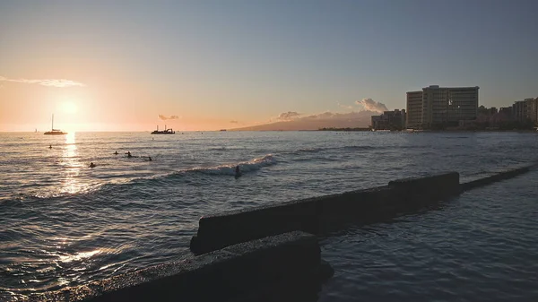 Geweldige kleuren van een tropische zonsondergang. Silhouetten van zeilboten die aan de oceaanhorizon drijven. Surfers rijden op de golven. Oahu, zomervakantie op Hawaï. Langzame beweging. — Stockfoto