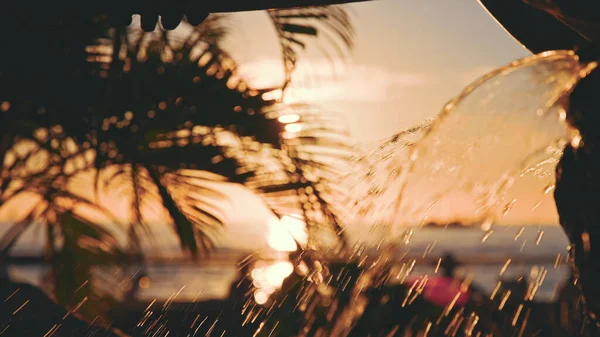 Fuente con agua dorada. Las hojas de un cocotero se balancean en el viento contra el cielo azul al atardecer. Increíblemente hermosa puesta de sol en la playa de Waikiki, Oahu, Hawaii. Imágenes De Stock Sin Royalties Gratis
