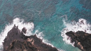 İHA 'dan hava görüntüsü. Kayalık okyanus kıyısının en üst manzarası. Pasifik Okyanusu 'nun Mavi Dalgaları kayaya çarpıyor. Beyaz deniz köpüğü. Tropik ada Oahu Hawaii 'nin volkanik plajı.