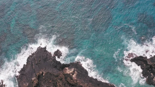 Letecký výstřel z dronu. Horní pohled na skalnaté pobřeží oceánu. Modré vlny Tichého oceánu padají na skálu. Bílá mořská pěna. Sopečná pláž tropického ostrova Oahu Havaj. — Stock fotografie