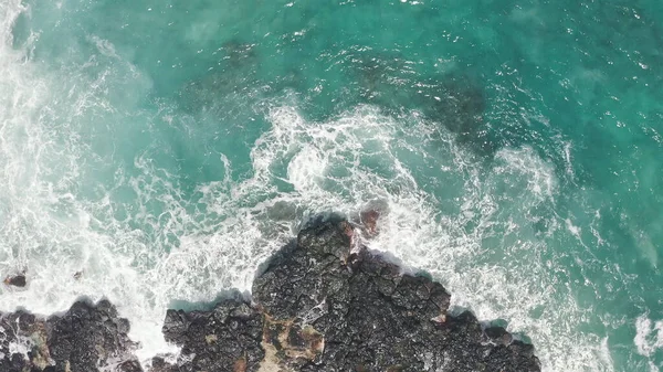 İHA 'dan hava görüntüsü. Kayalık okyanus kıyısının en üst manzarası. Pasifik Okyanusu 'nun Mavi Dalgaları kayaya çarpıyor. Beyaz deniz köpüğü. Tropik ada Oahu Hawaii 'nin volkanik plajı.