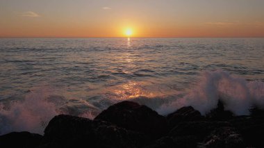 Dramatik okyanus batımı. Yanan gökyüzü ve parlayan altın dalgalar kayalara çarptı. Gün batımı denizi 4k. Martılar uçuyor. Kızıl gökyüzü, sarı güneş ve inanılmaz deniz. Yaz günbatımı deniz manzarası. Yavaş çekim.