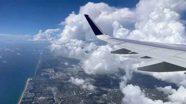 Flug über Miami. Blick auf die Ostküste aus dem Fenster des Flugzeugs. Schöne weiße Wolken vor blauem Himmel. Das türkisfarbene Wasser der Atlantikküste. — Stockfoto