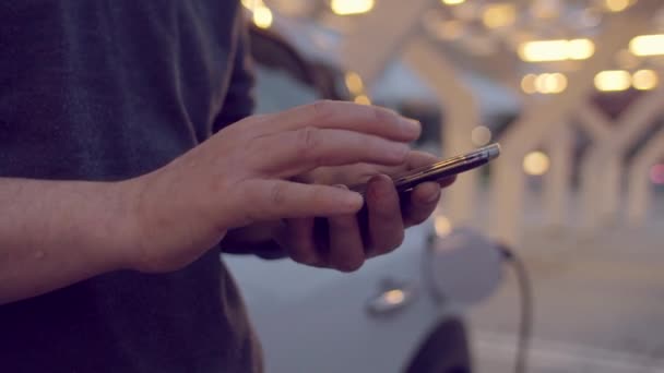 Hombre usando el teléfono inteligente mientras carga su coche eléctrico — Vídeos de Stock