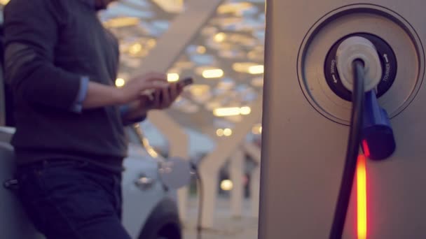 Hombre usando el teléfono inteligente mientras carga su coche eléctrico — Vídeo de stock
