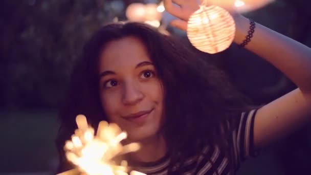 Повільний знімок молодої жінки, що освітлює блискітки в саду — стокове відео