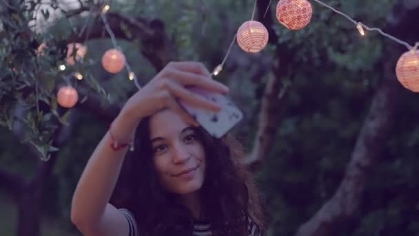Cámara lenta de la joven mujer tomando selfie bajo linternas — Vídeos de Stock